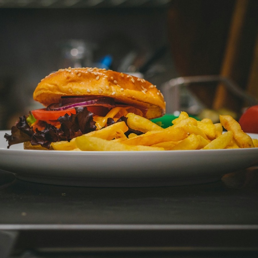Hamburguesa completa con papas fritas en un plato blanco, fotografiada de frente con luz cuidada