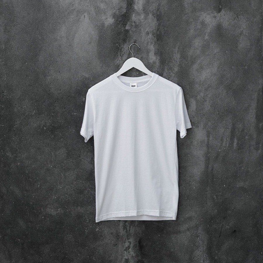 Remera blanca lisa colgada de una percha sobre una pared de cemento