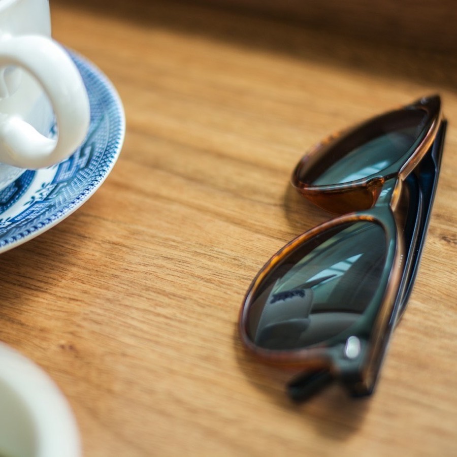 Anteojos de sol de marco carey sobre una mesa de madera, junto a una taza de té