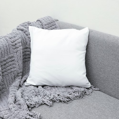 Almohadón blanco sobre un sillón gris con manta