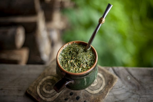 Mate de cerámica verde con yerba y bombilla sobre un posavasos de madera