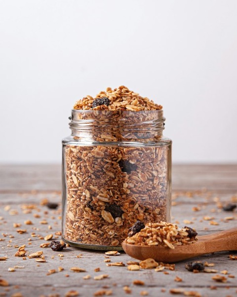 Frasco de vidrio lleno de granola junto a una cuchara de madera