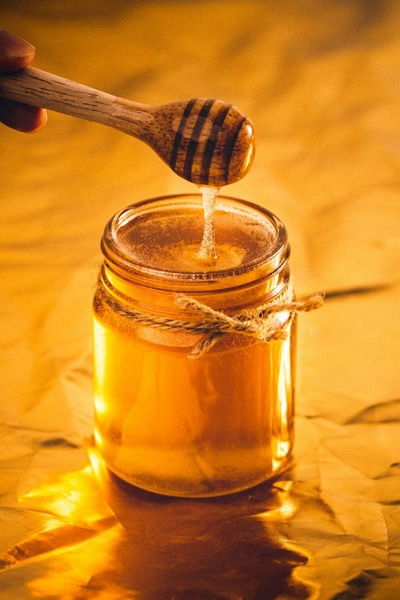 Frasco de miel con un cucharón de madera que gotea