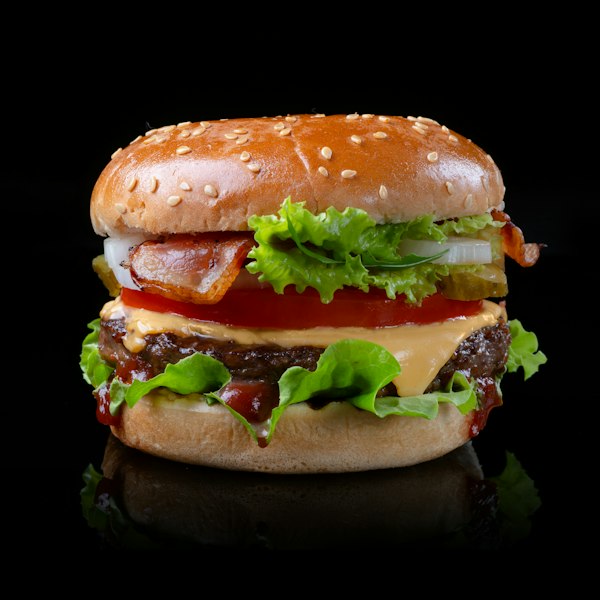 Hamburguesa con queso, lechuga y tomate sobre fondo negro