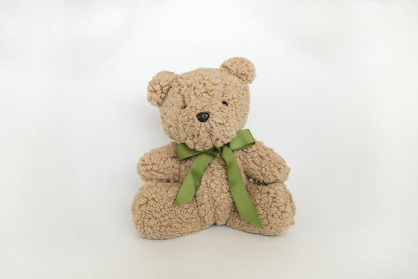 Oso de peluche con moño verde sobre fondo blanco