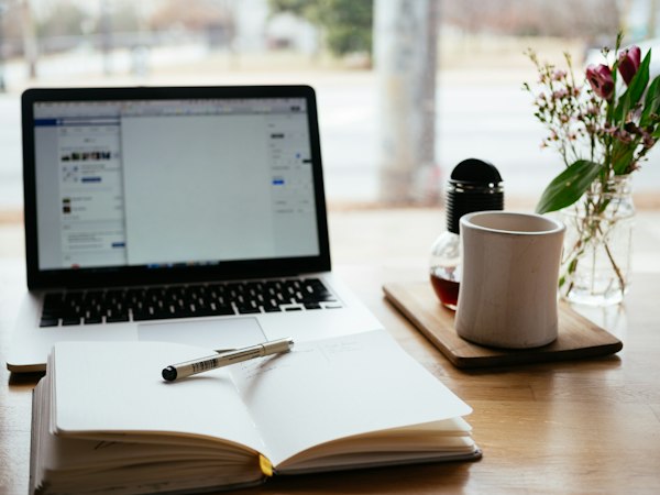 Laptop abierta junto a un cuaderno y una taza de café